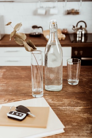 close up view of remote car key, bottle of water and branch in vase at wooden table in kitchen