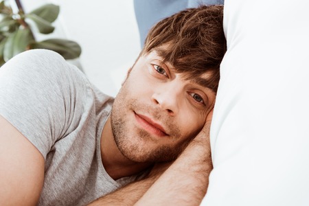 Close up portrait of man looking at camera and laying in bed at homeの写真素材