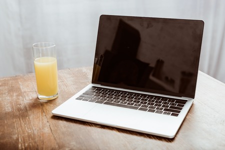 Close up view of laptop with blank screen and orange juice at tableの写真素材