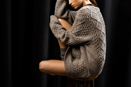 partial vie of woman in woolen grey sweater sitting on bar stool on black backgroundの写真素材