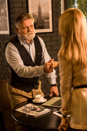 partial view of business partners shaking hands after business meeting in cafeの写真素材