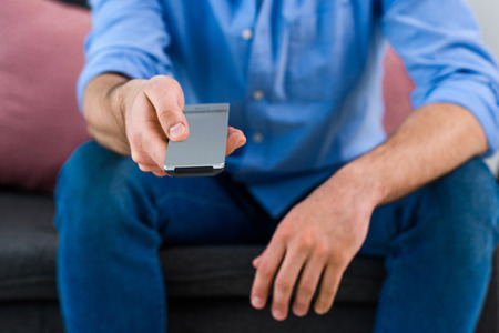 cropped shot of man changing channels while watching tv at home