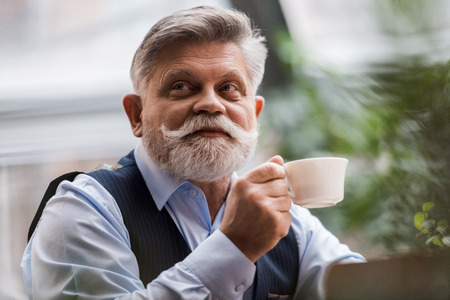 portrait of senior bearded man with cup of coffee in cafeの写真素材