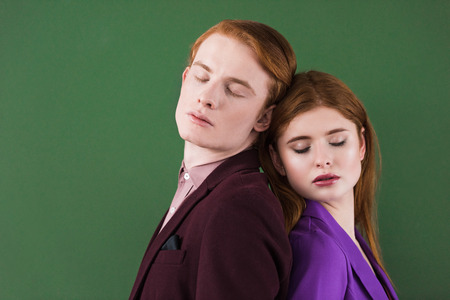 Young fashion models with closed eyes standing back to back isolated on green