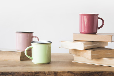 three colored cups and books on wooden table on whiteの写真素材