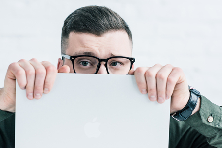 obscured view of businessman in eyeglasses covering face with laptopの写真素材