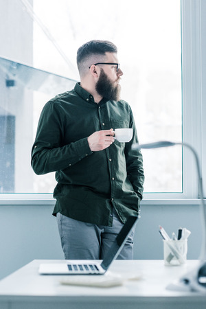 selective focus of pensive businessman with cup of coffee looking out windowの写真素材