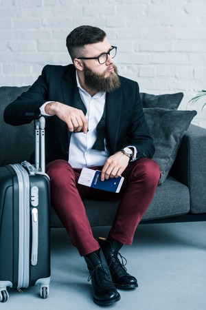 thoughtful businessman with passport, ticket in hand and baggage near by resting on sofaの写真素材
