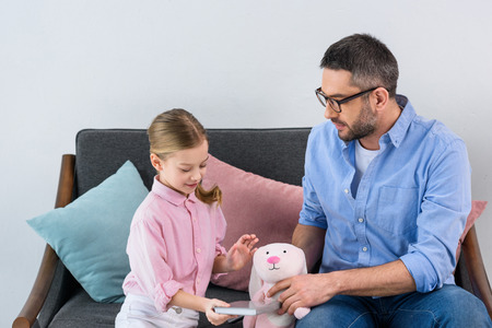 portrait of father playing with daughter with toy on sofa at homeの写真素材