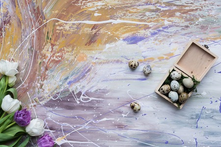 Quail eggs in box and tulips on stained background