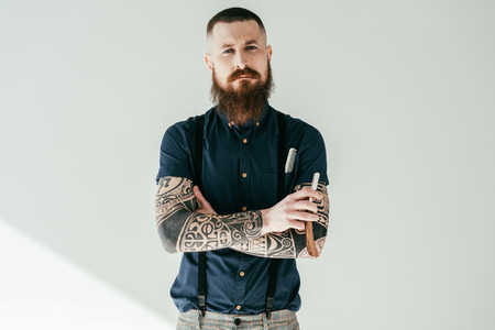 tattooed man holding razor and looking at camera isolated on whiteの写真素材