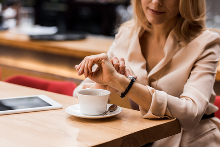 cropped shot of businesswoman checking time while sitting at table with tablet and cup of coffeeの写真素材