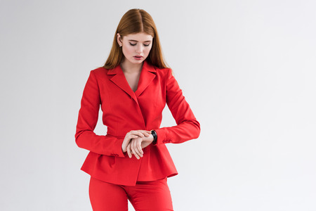 Young stylish female dressed in suit looking at wristwatch isolated on grey