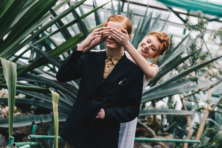 smiling redhead girl in white dress closing eyes to young man in botanical gardenの写真素材