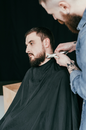 barber trimming customer beard at barbershopの写真素材