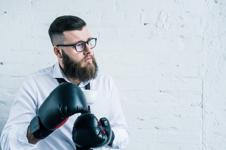 portrait of pensive businessman in boxing gloves holding cup of coffee