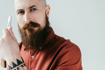 portrait of bearded handsome barber holding razor isolated on white