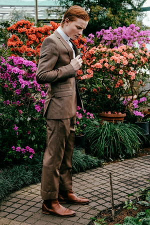 stylish young man with red hair in suit standing glasshouseの写真素材