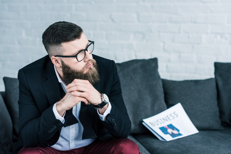 portrait of thoughtful businessman sitting on sofa with business newspaperの写真素材
