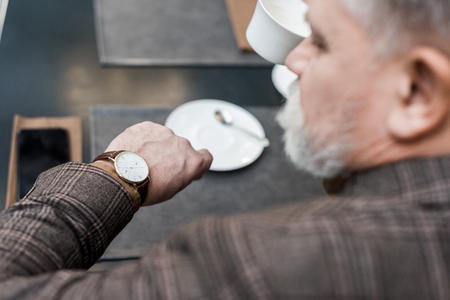 selective focus of senior businessman checking time while sitting at table in cafeの写真素材
