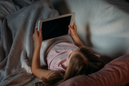 partial view of little kid using tablet in bed at homeの写真素材