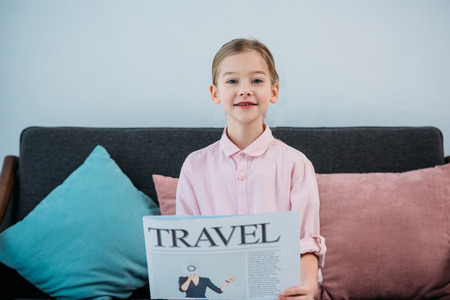 portrait of cute child with travel newspaper in hands sitting on sofa