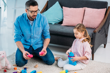 little daughter and father playing with colorful blocks together on floor at homeの写真素材