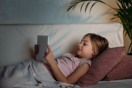 side view of little kid using tablet in bed at homeの写真素材