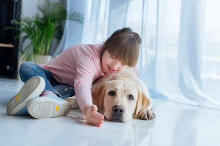 Child with down syndrome playing with Labrador retriever dog on the floorの写真素材