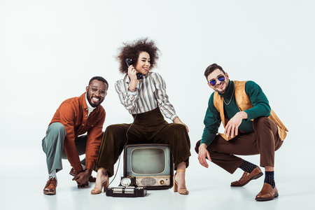 multicultural retro styled friends squatting with vintage television on whiteの写真素材