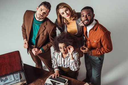overhead view of multicultural retro styled friends with typewriter looking at cameraの写真素材