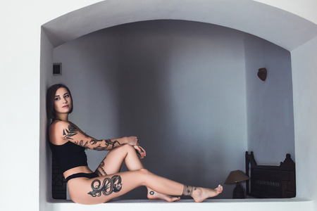 beautiful young tattooed woman in underwear sitting and looking awayの写真素材