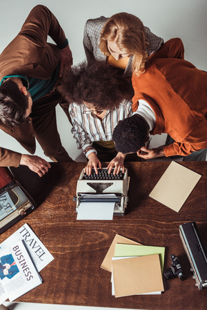 overhead view of multicultural retro styled journalists looking how friend typing textの写真素材