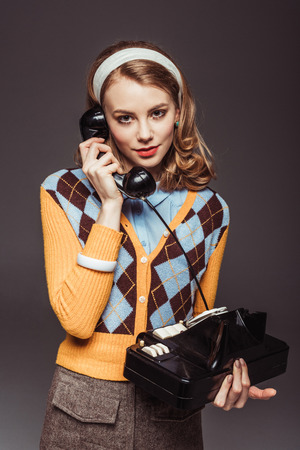 attractive retro styled girl talking by vintage stationary telephone isolated on greyの写真素材