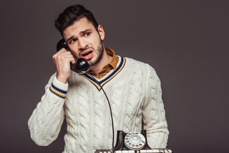 irritated retro styled handsome man talking by vintage stationary telephone isolated on greyの写真素材