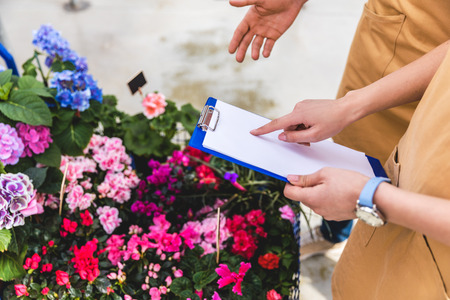 Close-up view of gardeners with clipboard discussing order in greenhouseの写真素材