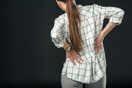 rear view of woman having pain in back, isolated on blackの写真素材