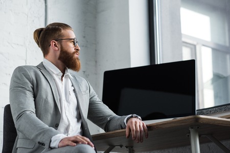 side view of businessman sitting at table with computer and looking awayの写真素材