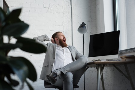 businessman yawning and sitting in chair in officeの写真素材