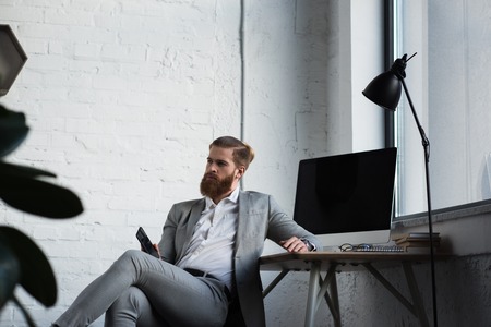 businessman sitting in chair, holding smartphone and looking awayの写真素材