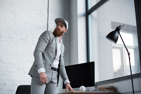 businessman in baseball cap looking away in officeの写真素材