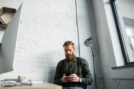 handsome bearded businessman using smartphone in officeの写真素材