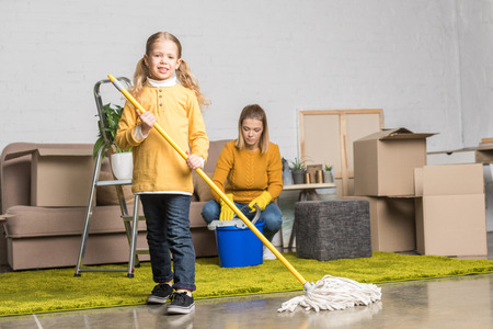 mother and daughter cleaning room with mop and bucket while moving home