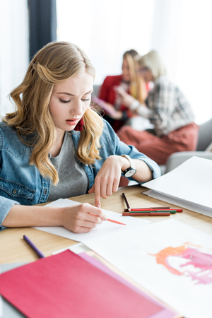 young blonde magazine editor drawing sketches in modern office, colleagues sitting behindの写真素材