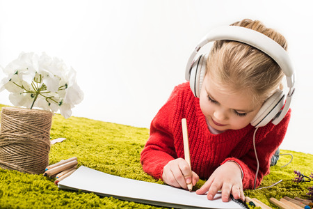 focused little child drawing with color pencils and listening music on green soft carpet isolated on whiteの写真素材