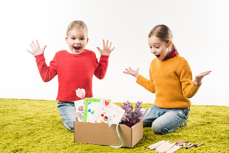 excited little sisters with box of materials for art sitting on floor isolated on whiteの写真素材