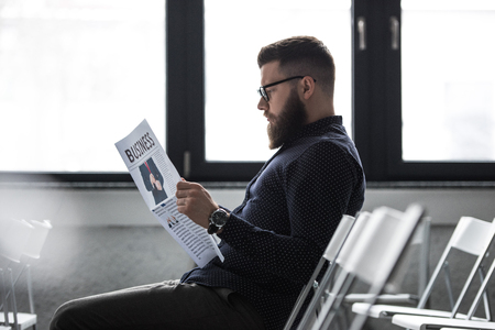 side view of focused businessman reading newspaper while sitting in meeting roomの写真素材