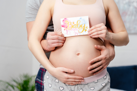 cropped shot of pregnant couple holding card with word babyの写真素材