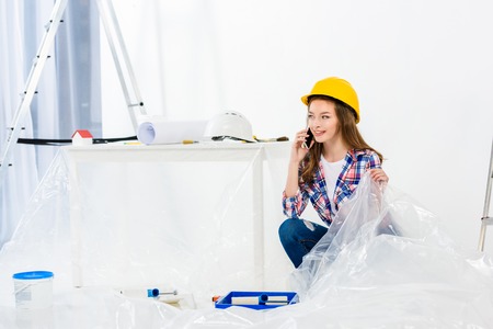 smiling girl in helmet sitting on floor and talking by smartphoneの写真素材