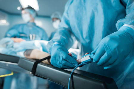 cropped image of doctor wearing pulse oximeter on patient finger in operating roomの写真素材